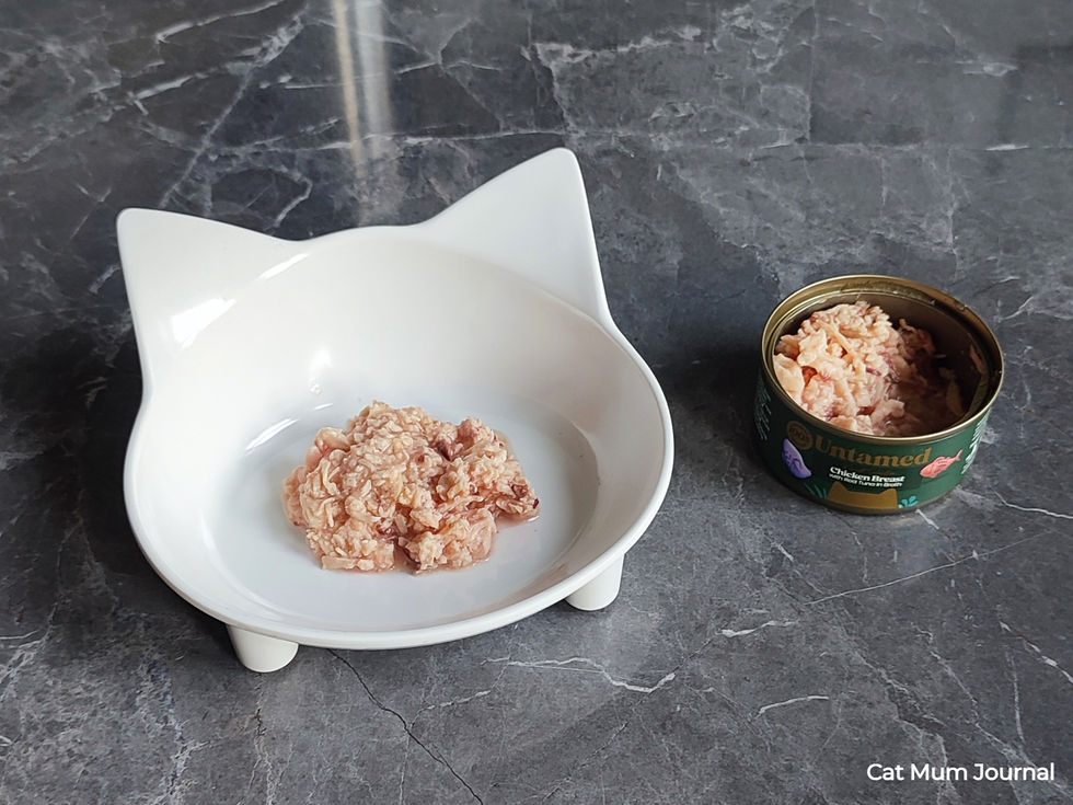 White cat food bowl next to an open tin of Untamed Chicken and Tuna in Broth.