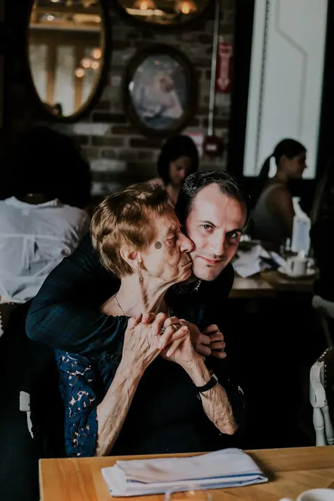 Groom to be hugging his grandmother from behind at his fiance's bridal shower