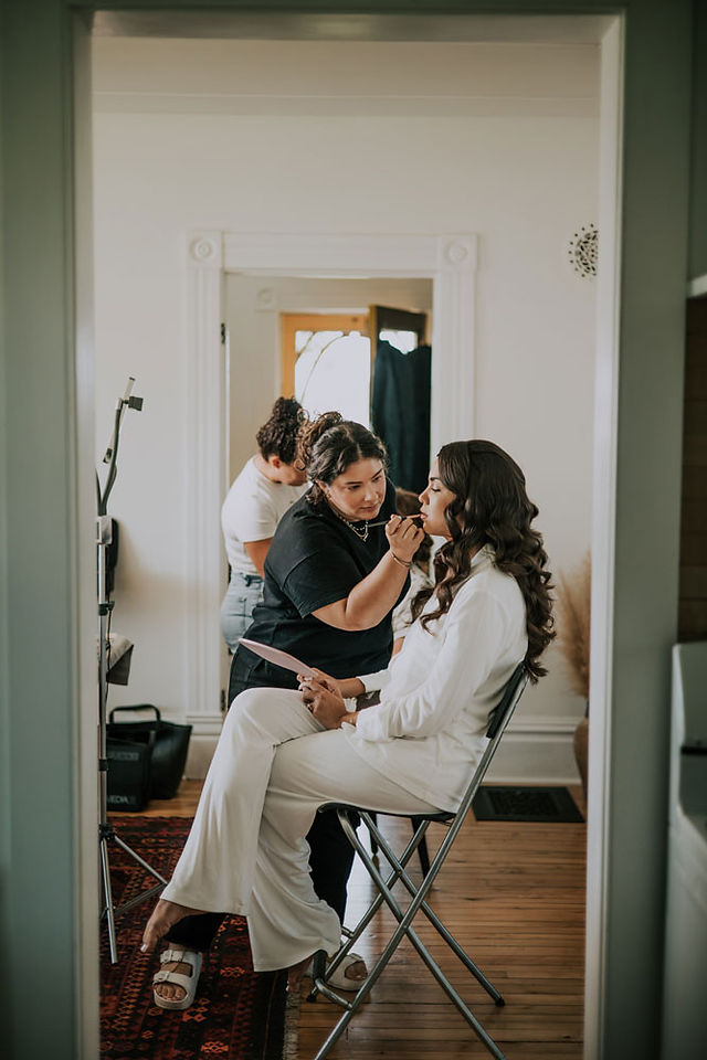 bride gets makeup on while sitting in her white pajamas