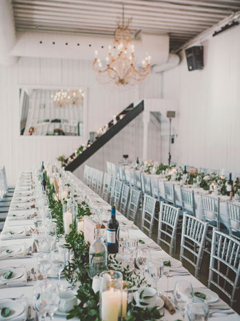 Long banquet table in a modern white venue with a lush greenery runner.
