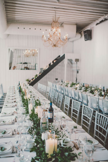 Long banquet table in a modern white venue with a lush greenery runner.