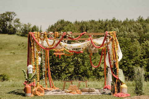 A mandap covered in orange, yellow and coral marigolds outside a farm setting