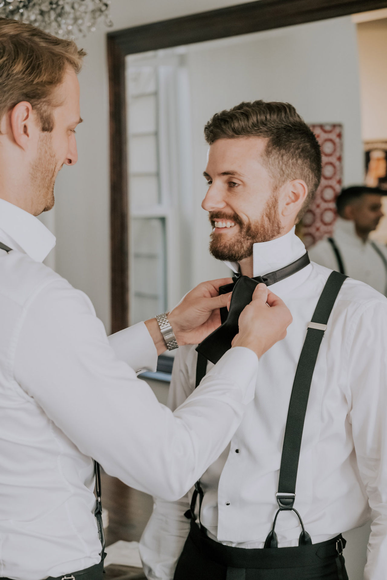 A man helps a groom attach his black bowtie