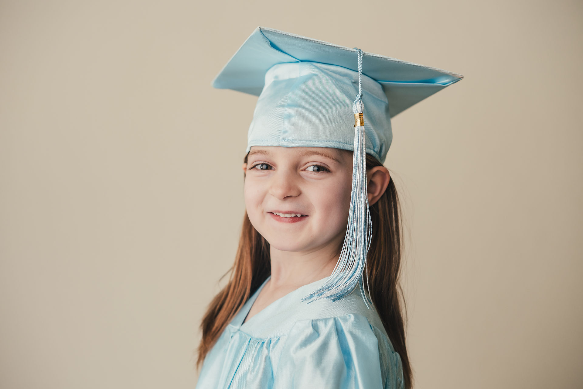 Young girl wearing cap and gown with long hair beneath her graduation cap