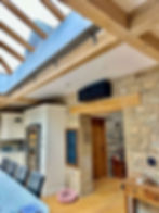 Wall-mounted air conditioning unit installed in kitchen with stone walls and wooden beams.”