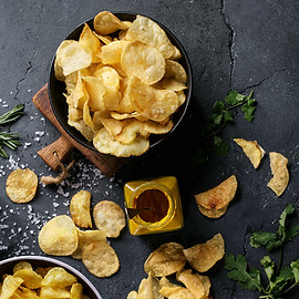 Bowl of home made potato chips served with mustard, rosemary, fleur de sel salt on stone b