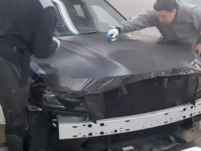 Two installers precisely glassing and squeegeeing a matte black vinyl wrap across the hood of a vehicle