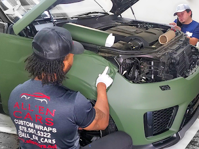 Instructor in an All’en Cars shirt teaching a student how to apply matte green vinyl wrap to a vehicle fender in a wrap class.
