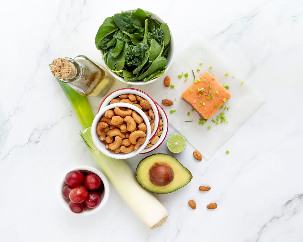 Top-down display of healthy foods with magnesium: spinach, salmon, nuts, avocado, grapes, leek, lime, and oil on a white marble surface.