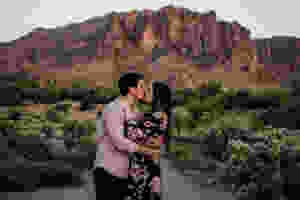 A couple kisses in front of Lost Dutchman State Park in Arizona during their adventure engagement session