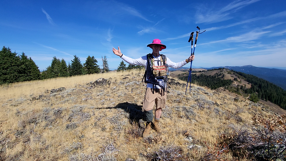 Glenn, host of Amputee Outdoors, at Observation Peak. He is wearing a wide brim sunhat, a chest pack for camera gear, and holding two hiking poles.