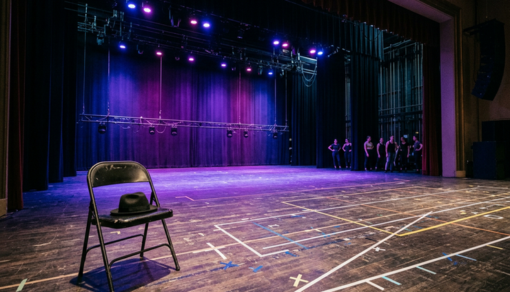 Wide-angle view of a theater stage glowing with purple light and rehearsal marks on the floor.