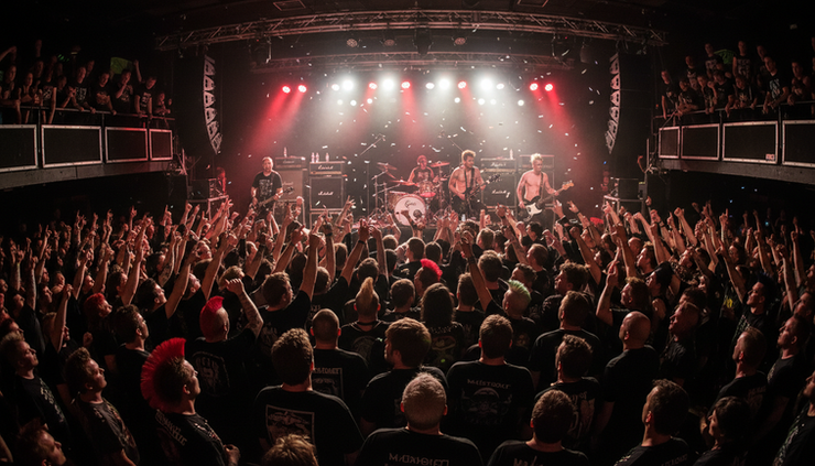 Wide-angle view of a punk rock crowd facing a brightly lit concert stage
