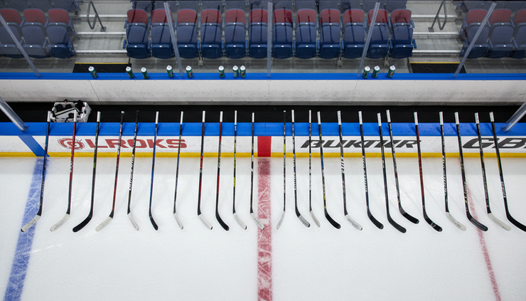 Overhead view of hockey sticks lined up beside a preseason bench