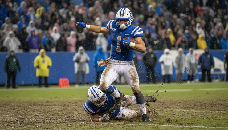 Eye-level view of a Kentucky running back breaking through a tackle on a rainy field.