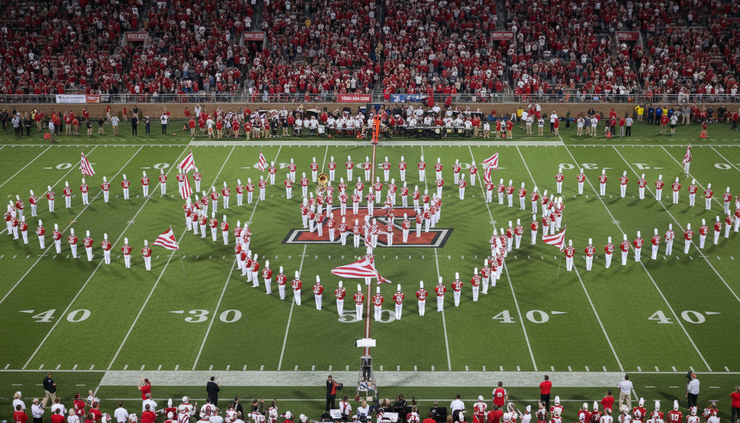 High-angle view of a marching band performing on a football field surrounded by red-clad fans