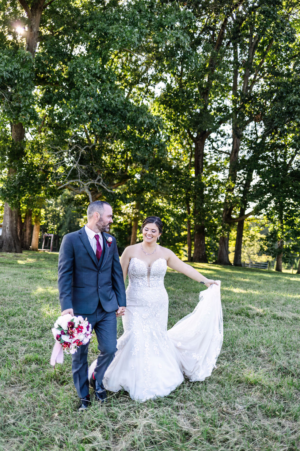 a bride and groom are walking in a field holding hands
