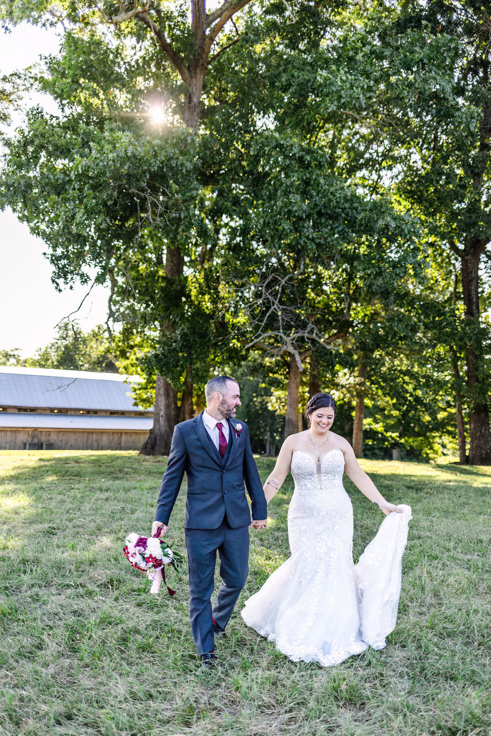 a bride and groom are walking in a field holding hands