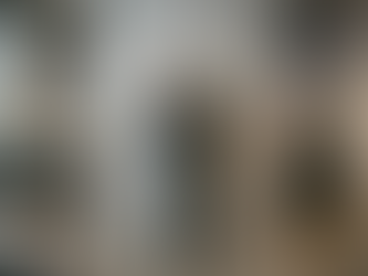 Hier ist der deutsche Alt-Text für das Bild: Alt-Text: Ein moderner Mann steht mit dem Rücken zum Betrachter direkt vor einer massiven, deckenhohen Betonwand in einem Agenturbüro. Er trägt ein dunkles Sakko, eine dunkle Jeans und braune Lederstiefel. Seine Hände liegen flach auf dem rauen Beton, während er den Kopf leicht in den Nacken legt und an der Wand nach oben blickt. Die Szene symbolisiert eine berufliche Blockade oder eine unüberwindbare Hürde. Im Hintergrund ist ein geschäftiges Großraumbüro im Industrie-Stil mit Ziegelwänden, großen Fenstern und arbeitenden Kollegen zu sehen. Auf einem Tisch im Vordergrund liegen Design-Bücher, unter anderem mit der Aufschrift „BAUHAUS“ und „DEEP WORK“. An einer Tür im Hintergrund hängt ein Schild mit der Aufschrift „STUDIO A - DEADLINE WALL IS FINAL“.