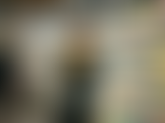 Ein junger, moderner Schwarzer Mann (PoC) steht sichtlich überfordert in einem Supermarkt vor einem prall gefüllten Kühlregal für Käse. Er trägt einen grauen Strickpullover und schaut mit einem gequälten, unschlüssigen Gesichtsausdruck auf drei Käsepackungen, die er in seinen Händen hält. Eine Hand führt er nervös zum Mund, während er die Produkte vergleicht. Im Hintergrund sind weitere Regale mit einer riesigen Auswahl an Käsesorten und andere einkaufende Personen in Unschärfe zu sehen. Die Szene verdeutlicht humorvoll das Phänomen der Entscheidungslähmung („Analysis Paralysis“).