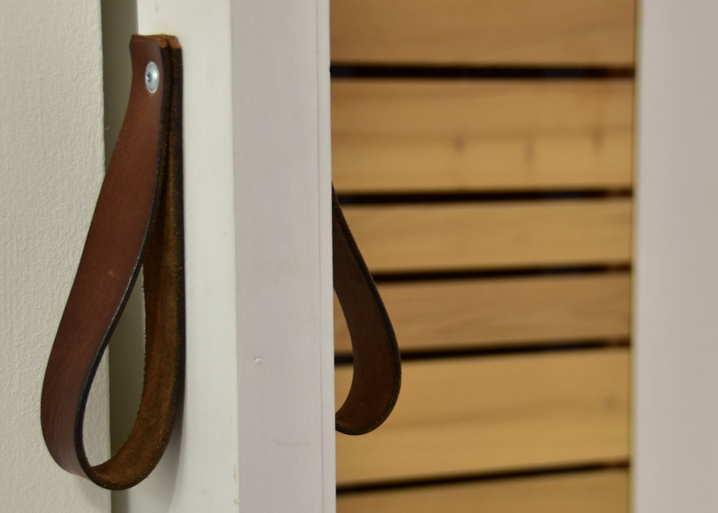 Lederschlaufe als Griff an einer hellen Holzfront mit Lamellen