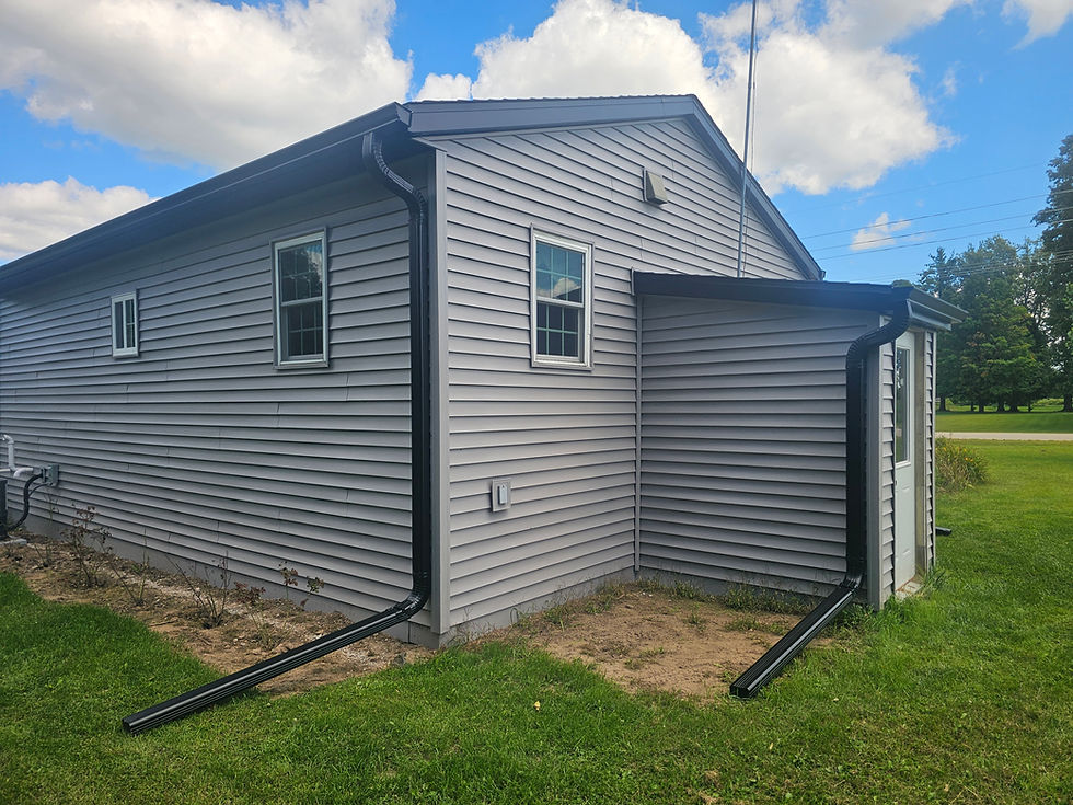 New black seamless gutters and downspouts installed on gray siding home