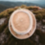 Thumbnail: A fawn alpaca felt hat sits on top of a grey mossy boulder hills in the background.