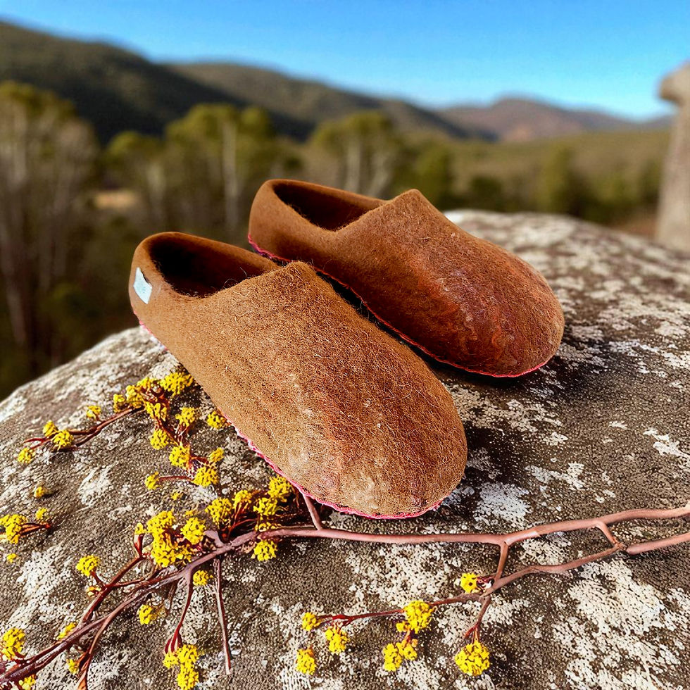 Thumbnail: A pair of brown toned alpaca felt slippers on a rock with some yellow wattle flowers and hills in the background.