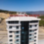 Hadriana Palace Hotel yazılı tabela, beyaz bina, yeşil dağlar ve mavi gökyüzü.