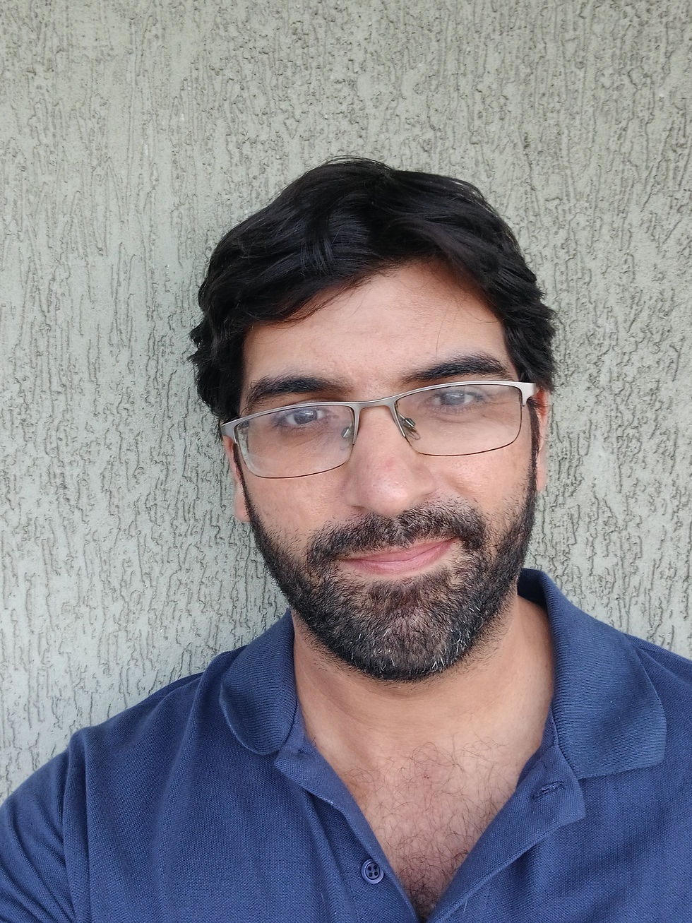 Homem de pele clara, olhos e cabelos escuros, barba curta e óculos de armação retangular