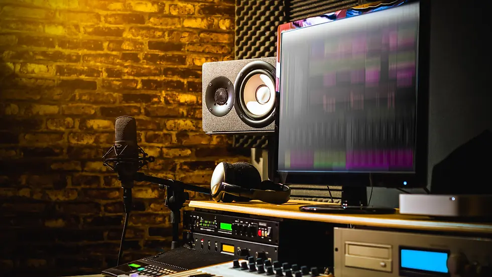 Recording studio with a microphone, speakers, and a monitor showing music software. Warm lighting, acoustic panels on brick wall background.