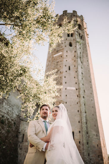 Bride and groom pose near a tall tower; Luxury Wedding at La Badia di Orvieto riccardopieri