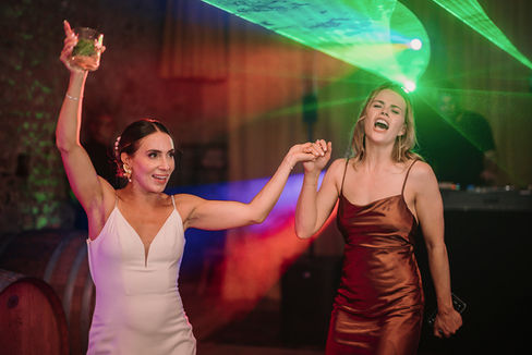 Bride and bridesmaid in rust dress dancing together under green laser beams.