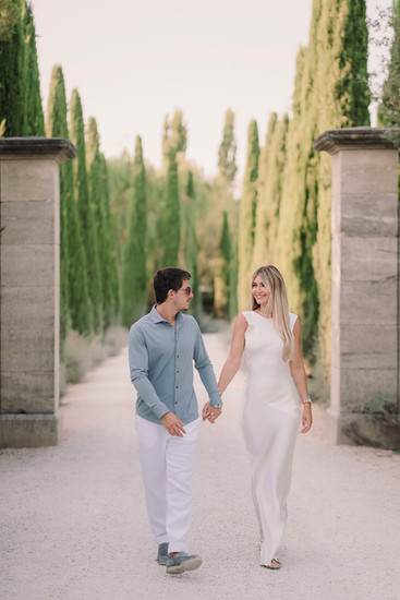Couple holding hands while walking between stone pillars and cypress trees in Tuscany, soft light and elegant romantic mood
