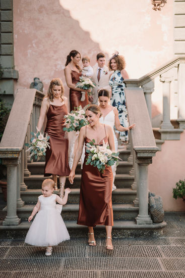 Wedding party descending stone stairs; bridesmaid holds flower girl's hand.