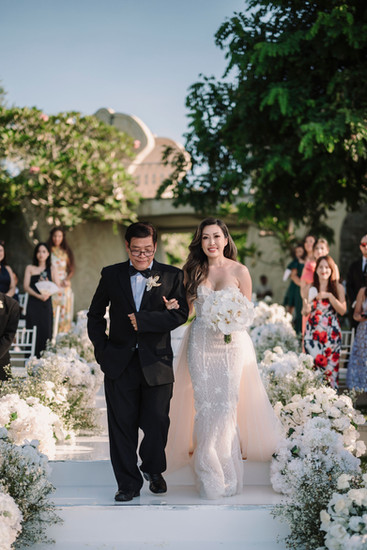 A father walks his daughter down the aisle at an outdoor wedding.