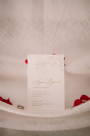 Wedding invitation with text Anya and Ray, flowers, and rings on white background.