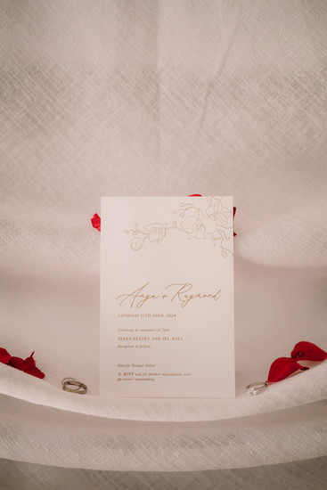Wedding invitation with text Anya and Ray, flowers, and rings on white background.