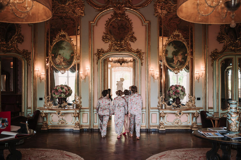 Bridesmaids in patterned pajamas walk through a grand room; luxury wedding at Ayana Resort Bali.