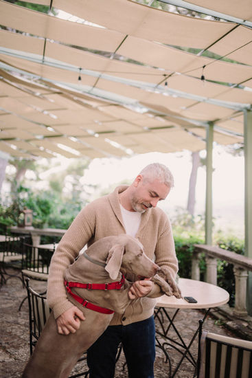Man holds dog, touching its face, tables, and outdoor setting riccardopieri
