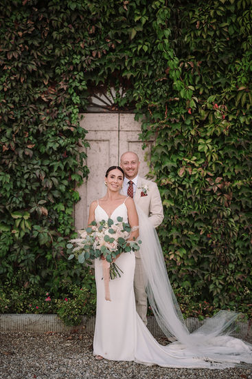Full-length portrait of the bride and groom against an ivy wall.