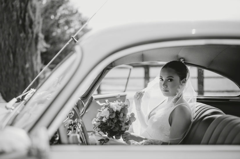 Bride lifting her veil and looking out the window from inside the vintage car.