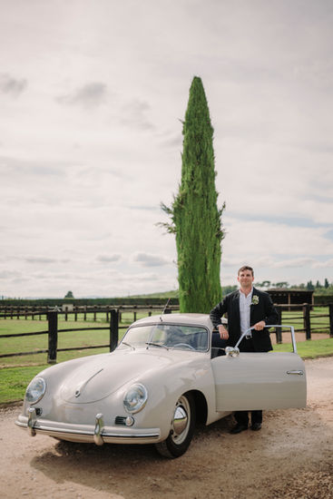 Groom standing beside the vintage car in the Tuscan countryside.
