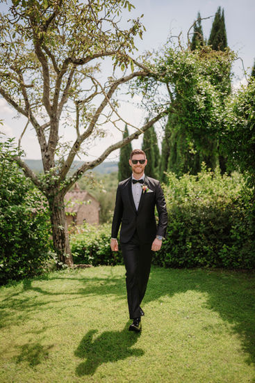 Groom in black suit walks towards camera on grass; Jessica and Liam – Tuscan wedding.