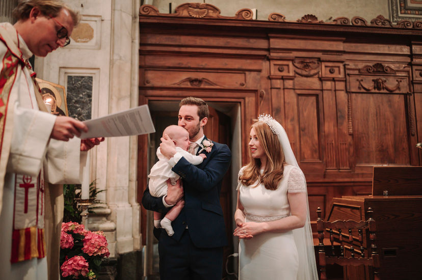 Priest reading during christening, man holding baby, woman smiling, elegant elopement at Belmond Villa San Michele Florence.