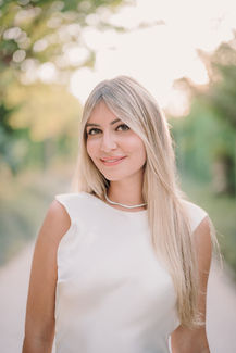 Blonde woman in white dress smiles, standing on a path riccardopieri
