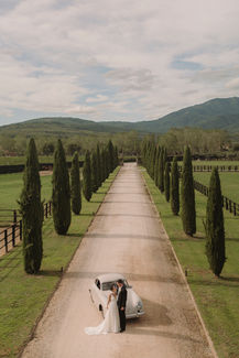 Aerial view of the bride and groom with vintage car on the cypress-lined avenue at Il Borro.
