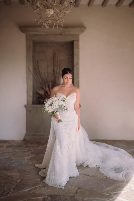 Bride in fitted wedding gown with bouquet under stone arch at Castello di Vicchiomaggio, Chianti