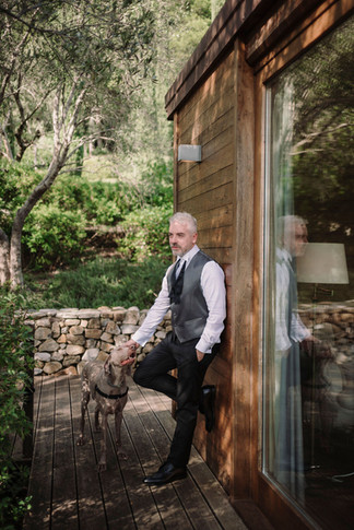 Uomo elegante con cane al guinzaglio, appoggiato a cabina in legno.