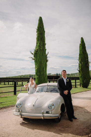 Bride and groom posing next to their vintage car in the Tuscan countryside.